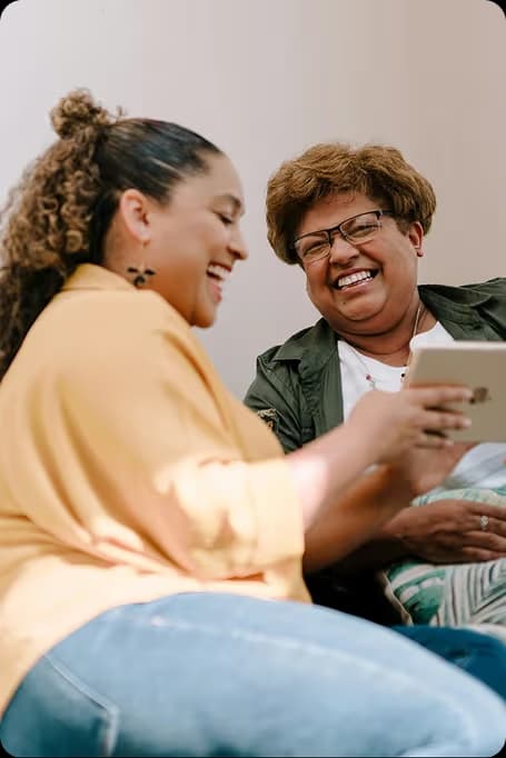 two women laughing over a tablet